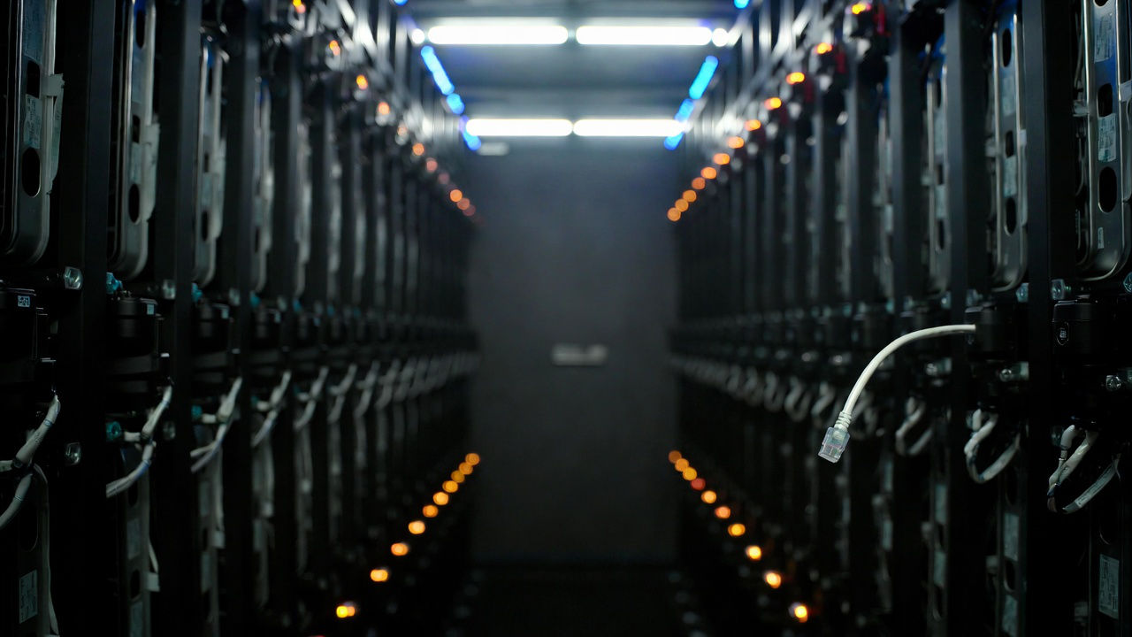 Resilienza operativa DORA: cavo ethernet scollegato in un corridoio di server rack con luci ambra intermittenti in una sala CED istituzionale.